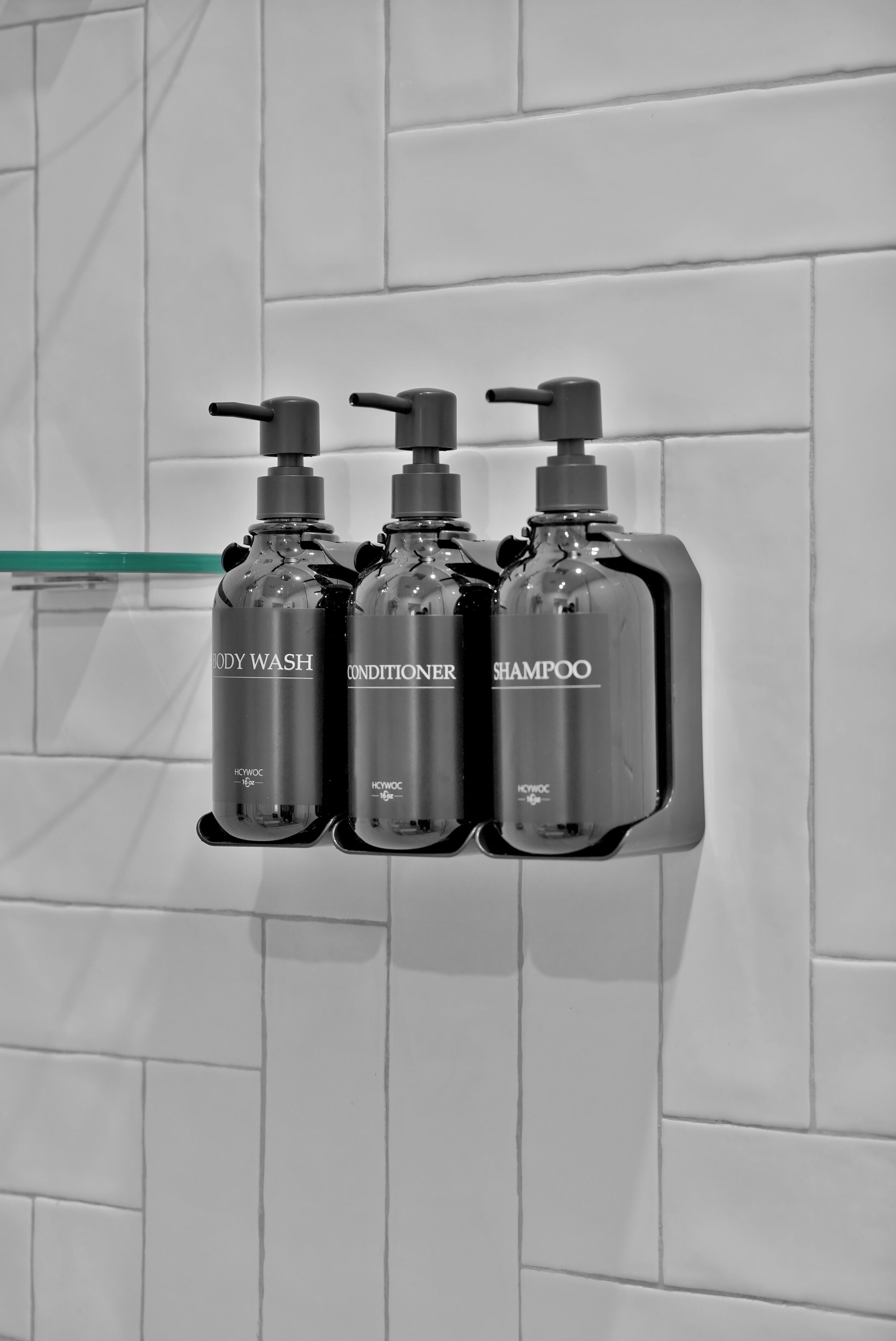 Tres botellas de artículos de tocador montadas en una pared con las etiquetas 'BODY WASH', 'CONDITIONER' y 'SHAMPOO'.