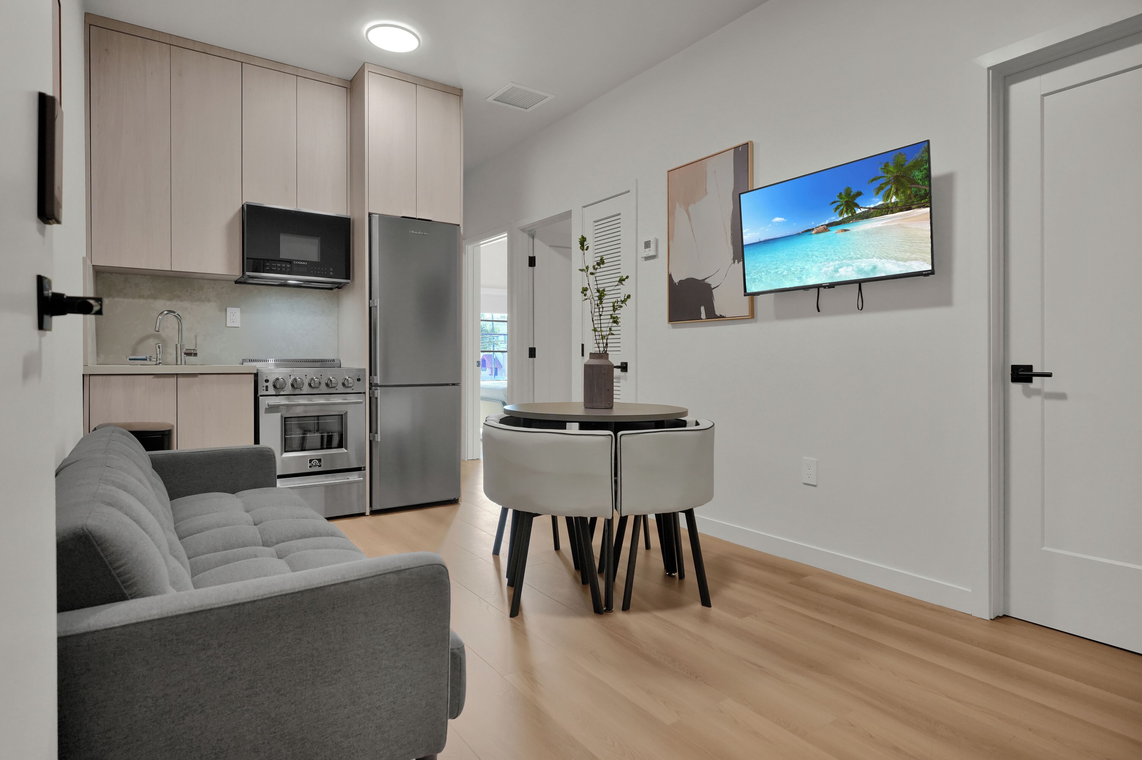 A modern kitchen with stainless steel appliances, a gray sofa, and a dining table with chairs.