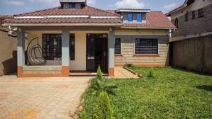 A two-story house with a tiled roof, a covered porch, and a small garden.