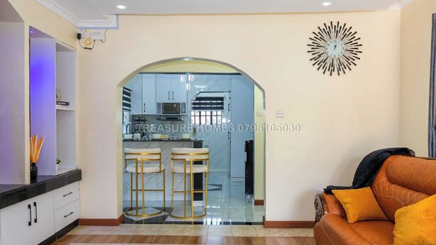 A modern living room with a sofa, a kitchen visible through an archway, and a decorative wall clock.