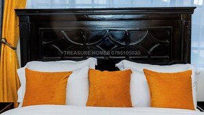 A hotel room with a dark wooden headboard, white bedding, and orange pillows.