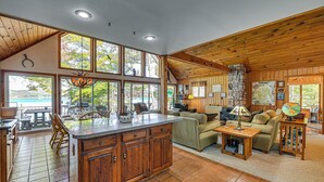 Un salón amplio con un gran techo de madera, una cocina con armarios de madera y vistas al exterior a través de amplias ventanas.