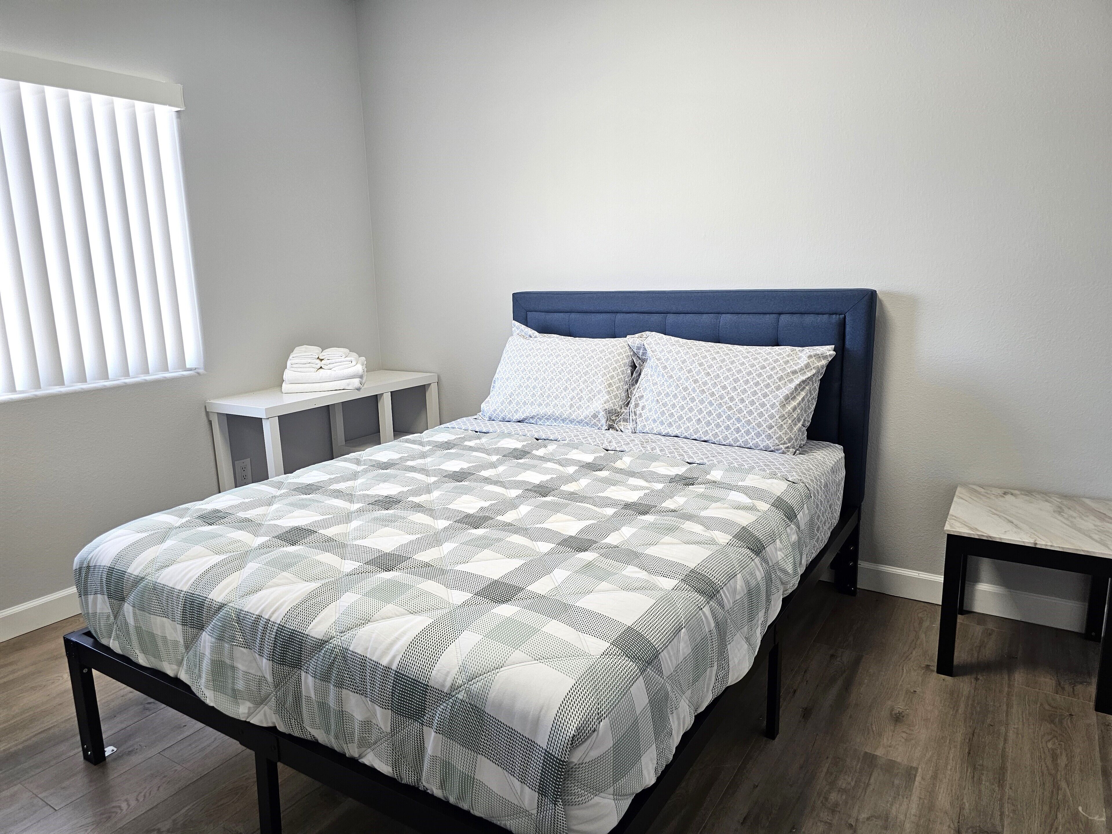 Una cama bien tendida con una colcha de estampado geométrico, un cabecero tapizado en azul y dos almohadas a juego.