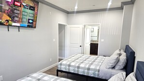 Un dormitorio con dos camas, un televisor instalado en la pared y una puerta que da al baño.