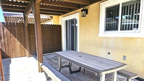 Un patio techado con una mesa y bancos de metal, una cerca de madera y una ventana con cristales de seguridad.