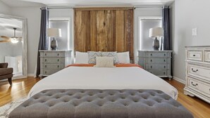 A bedroom with a large bed, two nightstands, a wooden headboard, and a grey ottoman. - The Given House - Modern Midtown Stay (Memphis)