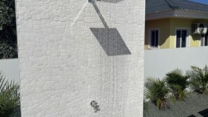 A modern outdoor shower with a textured wall and a sloped roof.