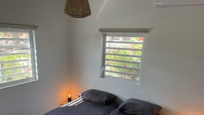 A bedroom with a bed, two windows, and a bedside table with a lamp.