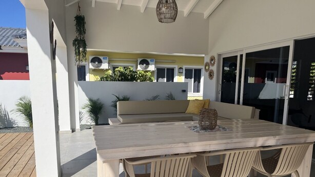 An outdoor patio with a wooden table and four chairs, a beige sofa, and a hanging plant.