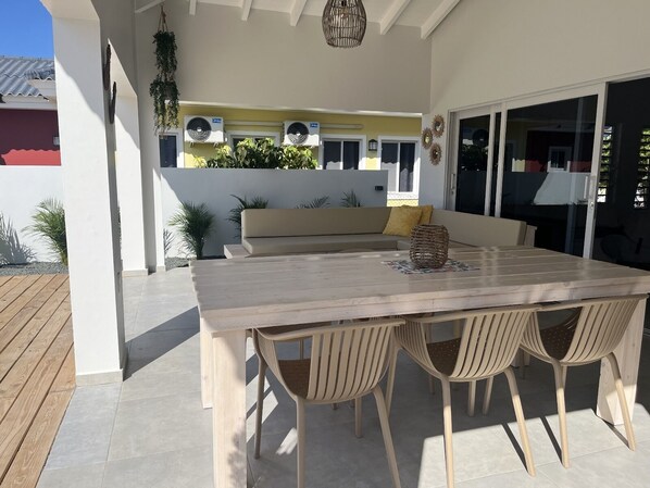 An outdoor patio with a wooden table and four chairs, a beige sofa, and a hanging plant.