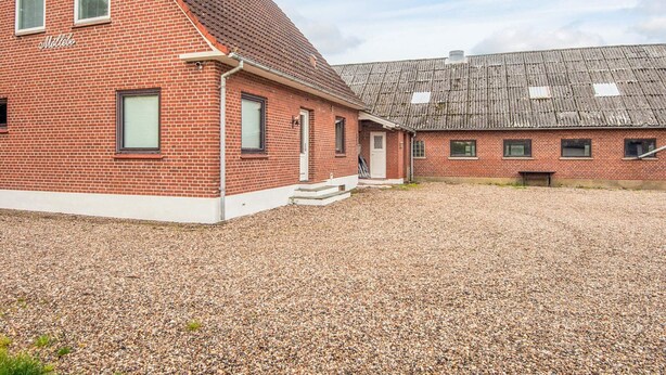 Een gebouw van rode bakstenen met een schuin dak en een grindpad, onder een heldere lucht.