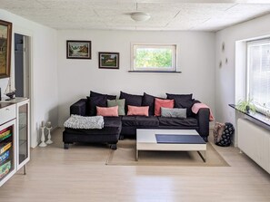 A living room with a black sofa, a coffee table, and a bookshelf. There are two framed pictures on the wall and a window with blinds.