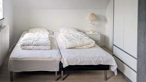 Een kleine eenpersoonskamer met twee eenpersoonsbedden, een nachtkastje met lamp en een radiator.