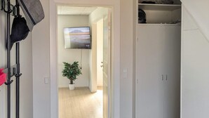 Een gang met een potplant, een televisie aan de muur en een garderobe.