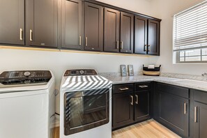 A laundry area with a washing machine and dryer, dark cabinets, a countertop, and a window with blinds. - Avondale Escape with amenities for your relaxation (Tolleson)