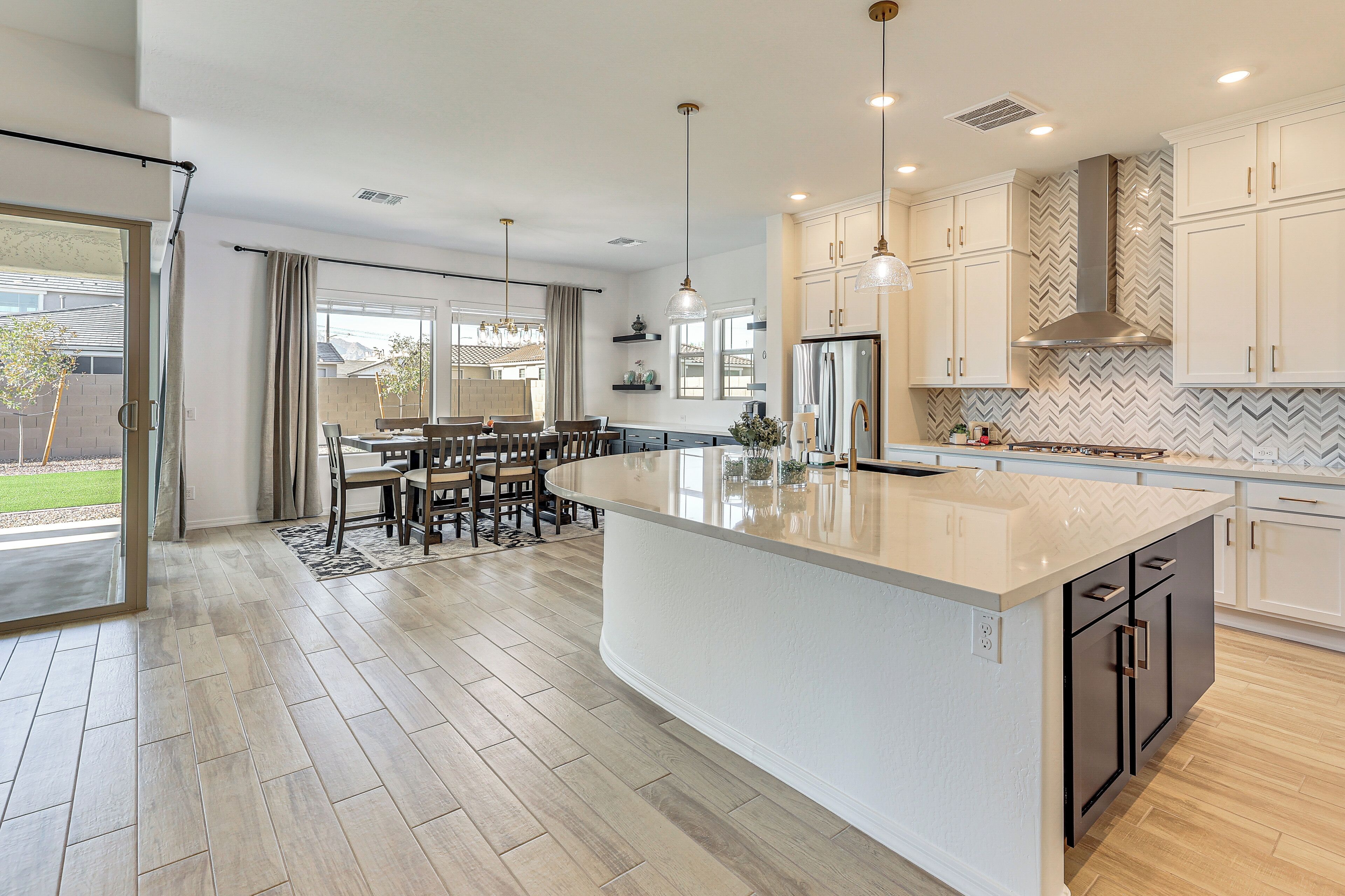 A modern kitchen with a large island, white cabinetry, and a herringbone tile backsplash.