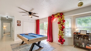 A pool table in a room with a ceiling fan, a cabinet with glass doors, and a view of the outdoors through windows. - Walk to Campus, FSU Photo Wall: Inviting Retreat! (Tallahassee)