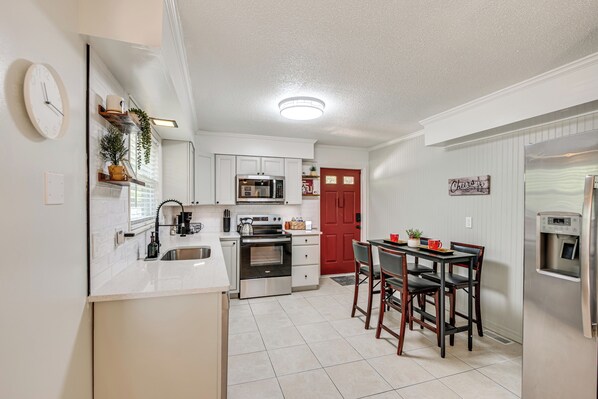 A modern kitchen with white cabinetry, a red door, and a dining area with wooden chairs. - Walk to Campus, FSU Photo Wall: Inviting Retreat! (Tallahassee)