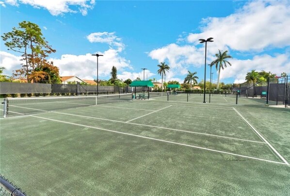 Un court de tennis extérieur doté d’un revêtement vert, d’un filet et d’une clôture périphérique.