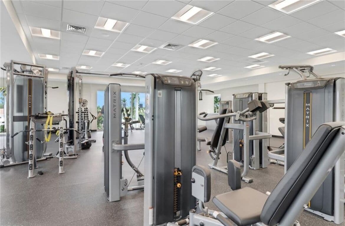 Ein Fitnessstudio mit verschiedenen Trainingsgeräten, darunter Gewichtbänke und Kurzhanteln, in großzügigem Raum.