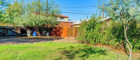 A residential backyard with a wooden fence, a tree, and a house with a red roof.