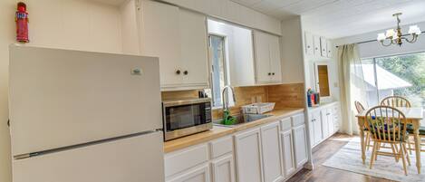 A kitchen with white cabinets, a microwave, a sink, and a dining area with a table and chairs.