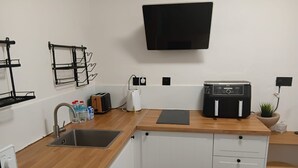 A compact kitchen with a wooden countertop, a built-in dishwasher, a toaster, a kettle, and a flat-screen TV mounted on the wall.