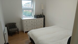 A bedroom with a bed, a dresser, a chair, and a radiator.