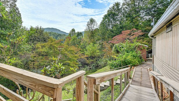 Eine Holzterrasse führt zu einem Haus mit Blick auf einen bewaldeten Hang.