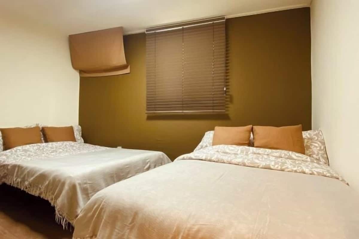 A bedroom with two beds, a window with blinds, and a wall-mounted light fixture.