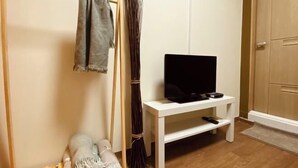 A room with a white TV stand, a flat-screen TV, a wooden door, and a woven basket. - Hideout Guesthouse (Seoul)