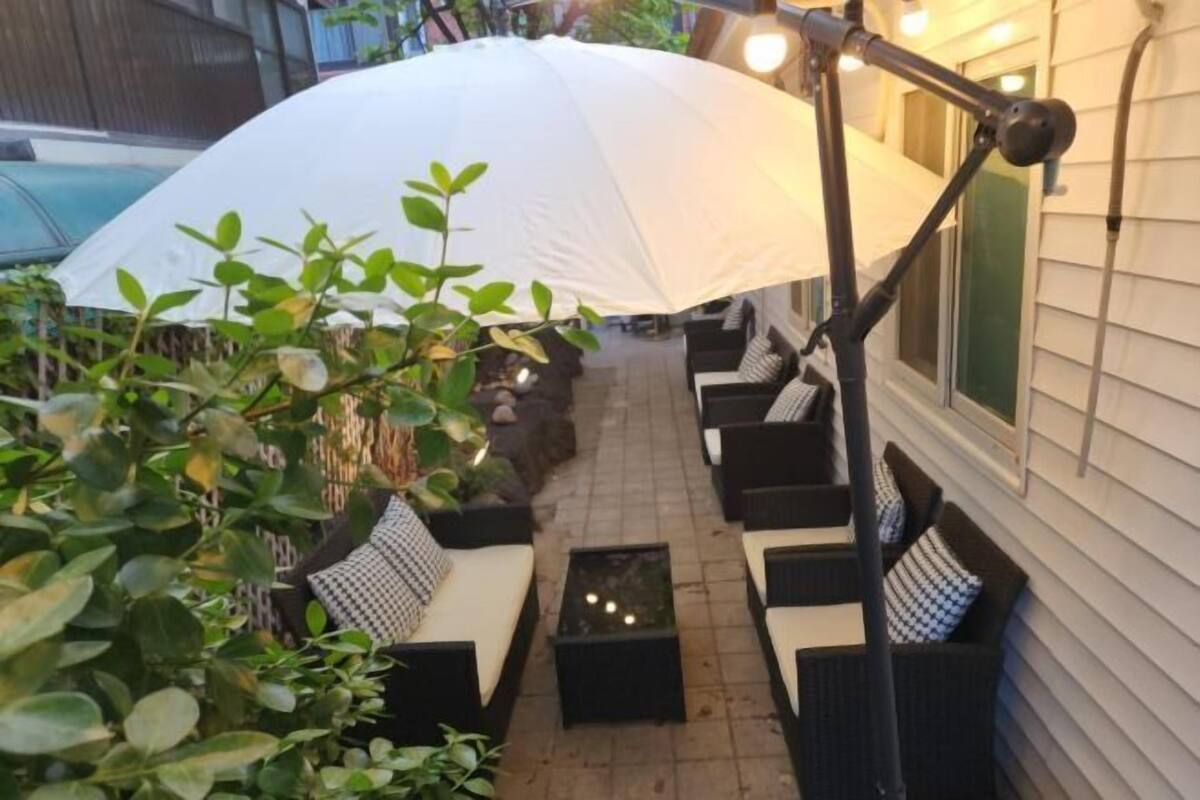 A patio with outdoor furniture, a white umbrella, and a pathway leading to a building.