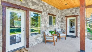 A covered patio with stone walls, wooden beams, and two cushioned chairs. - Beautiful 4 bedroom mountain retreat , with stunning views. (Buena Vista)