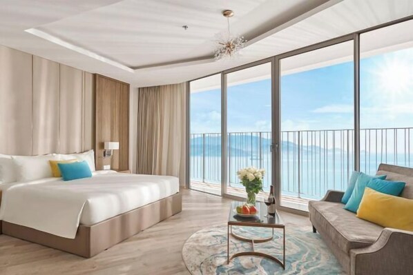 A hotel room with a large bed, a sofa, a small table with a vase, and a view of the sea.