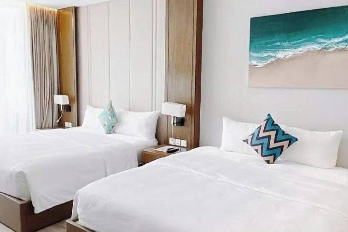Camera d'albergo con due letti, una testiera in legno, un quadro raffigurante una spiaggia e un comodino con una lampada.
