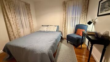A bedroom with a bed, a chair, a desk, and a lamp.