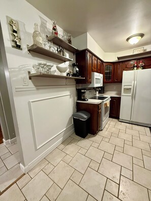 A kitchen with white cabinetry, a microwave, a refrigerator, and a trash bin.
