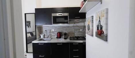 A compact kitchen with black cabinets, a microwave, a gas stove, and a hanging light fixture.
