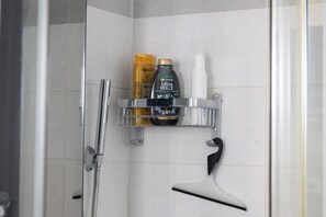 A shower area with a chrome showerhead, a handheld shower attachment, and a shelf holding toiletries including a bottle of shampoo and a bottle of lotion. - Nicla's Home (Rome)