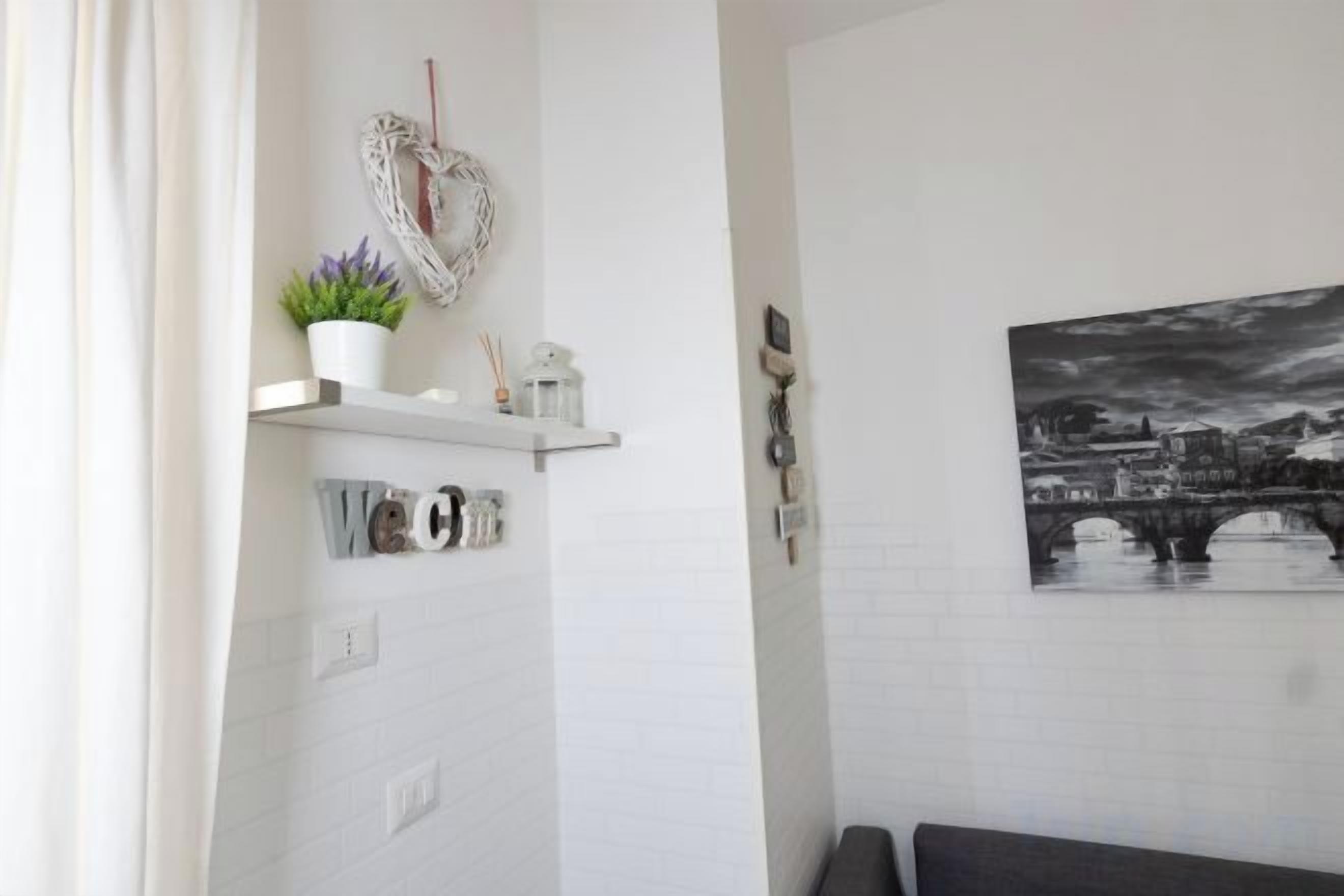 A bathroom with a white tiled wall, a heart-shaped decoration, a shelf with a plant, and a cityscape painting.