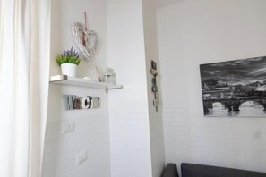 Ein Badezimmer mit weiß gefliesten Wänden, einer herzförmigen Dekoration, einem Regal mit Pflanze und einem Stadtbildgemälde.