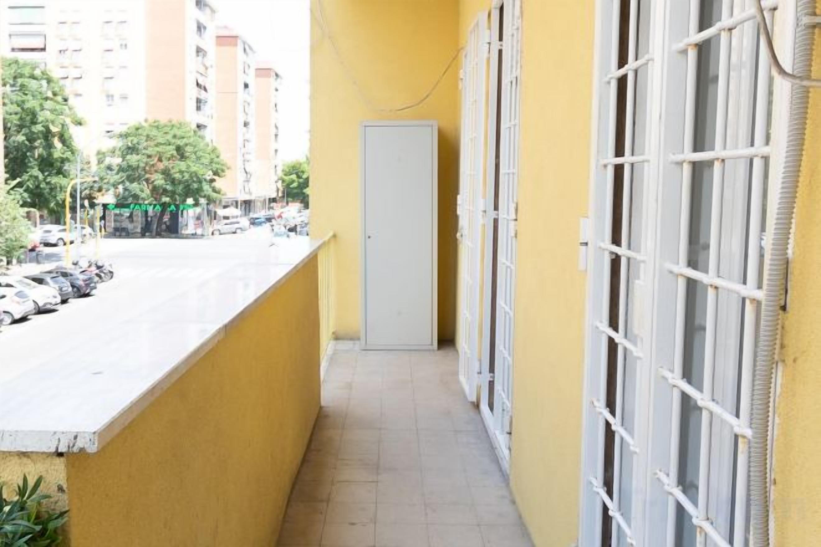 A narrow balcony with a view of a street and parked cars.