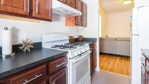 A kitchen with wooden cabinets, a white stove, and a grey sofa in the background. - Charming 1-bedroom apartment in Brooklyn with Projector, 25 mins to Manhattan (Brooklyn)