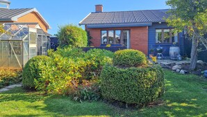 A residential house with a well-maintained garden, a greenhouse, and a barbecue area.