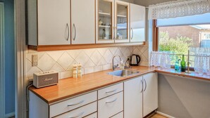 A kitchen with white cabinets, a wooden countertop, a sink, and a window with lace curtains.