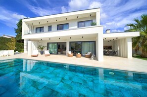 Et moderne hus med to etager, en swimmingpool, udendørs møbler og en patio.
