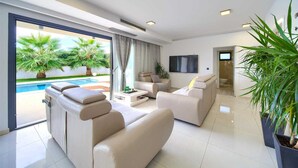 A modern living room with a pool view, a flat-screen TV, and a large potted plant. - Villa LUMINOSA with outdoor and indoor pool and sauna (Vrh)