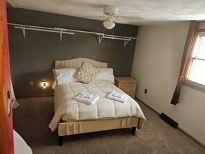 Un dormitorio con cama, mesitas de noche, ventilador de techo y ventana con cortinas.