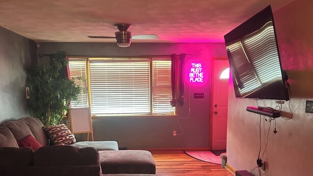 Una sala de estar con un sofá, un televisor montado en la pared y un ventilador de techo.