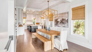 Una cocina moderna con armarios blancos, una mesa de comedor de madera con bancos y una lámpara colgante.